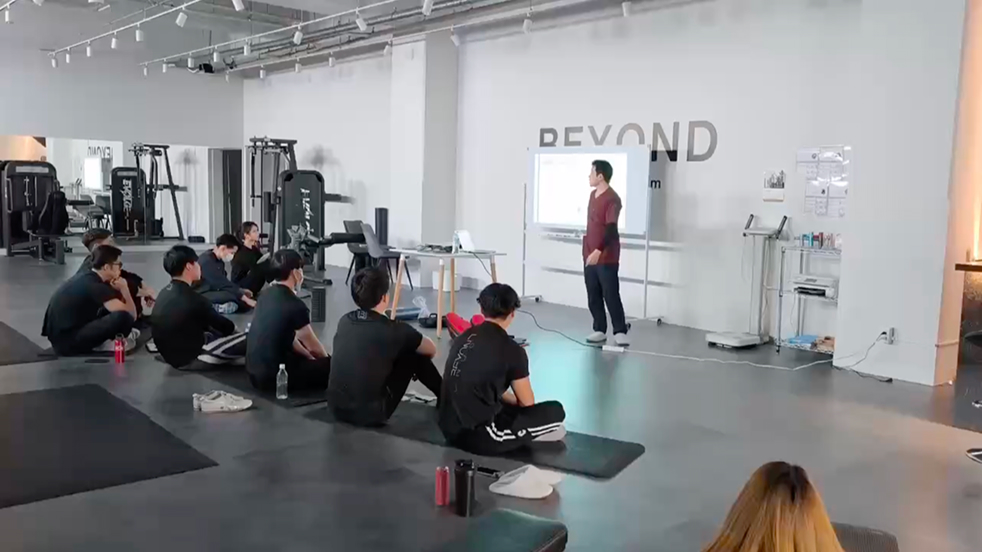 講師が大型モニターで人体解剖図を説明し、受講生全員がタブレットで同じ資料を確認しながら学ぶ研修風景